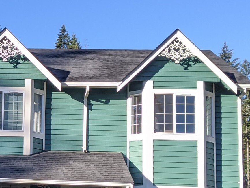 A teal house with white trim and decorative gable ornaments. 