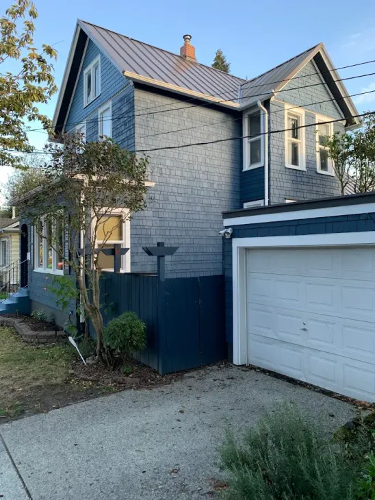 Two-story blue house with garage, white trim, and a gravel driveway at dusk