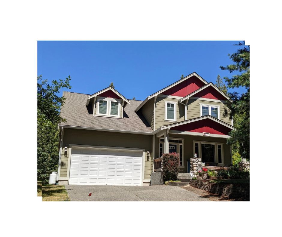 Front view of a green two-story house with a white garage door and trim, and red accent colors on the gable ends and dormer.