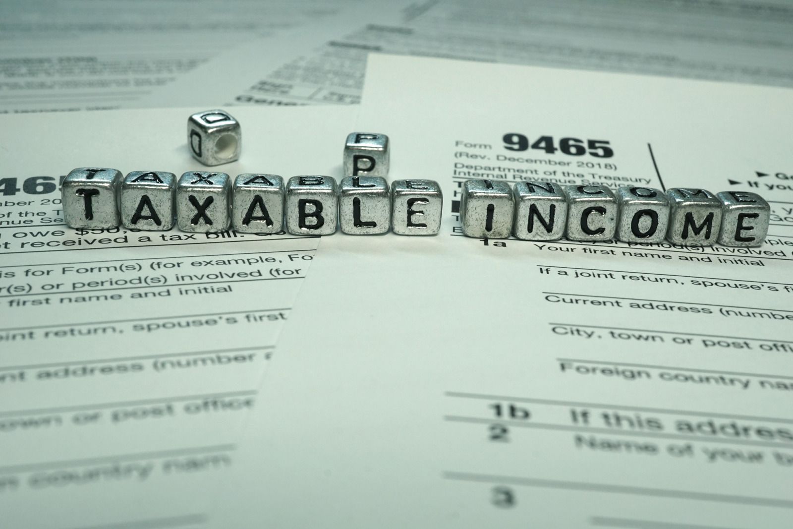 Letter tiles spelling “TAXABLE INCOME” on tax forms with a calculator in the background