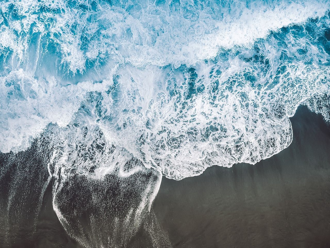 Vibrant blue waves meeting a dark sandy shore