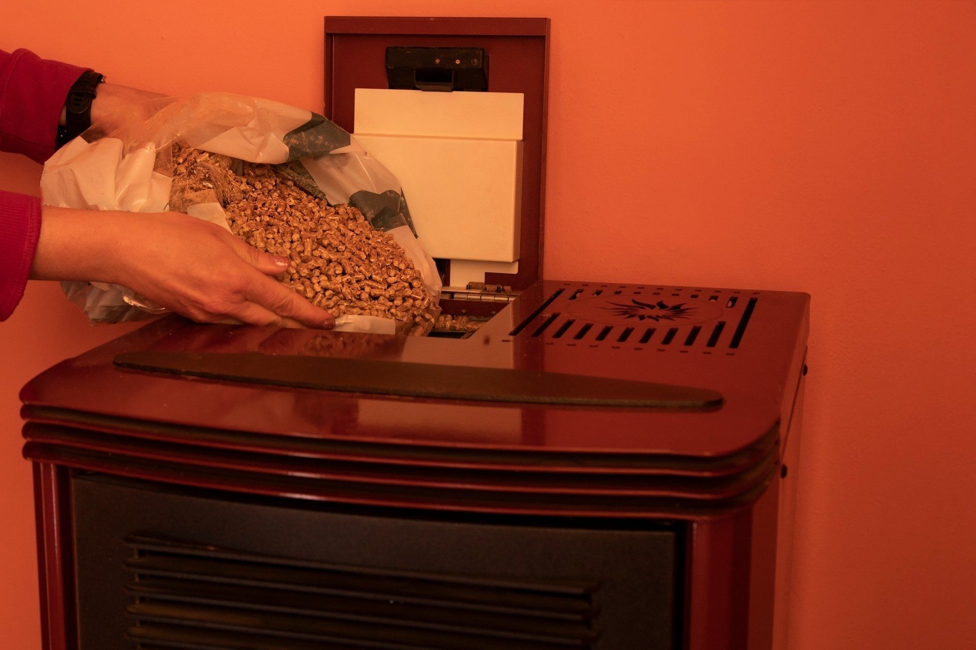 A person loading a hopper of a pellet stove