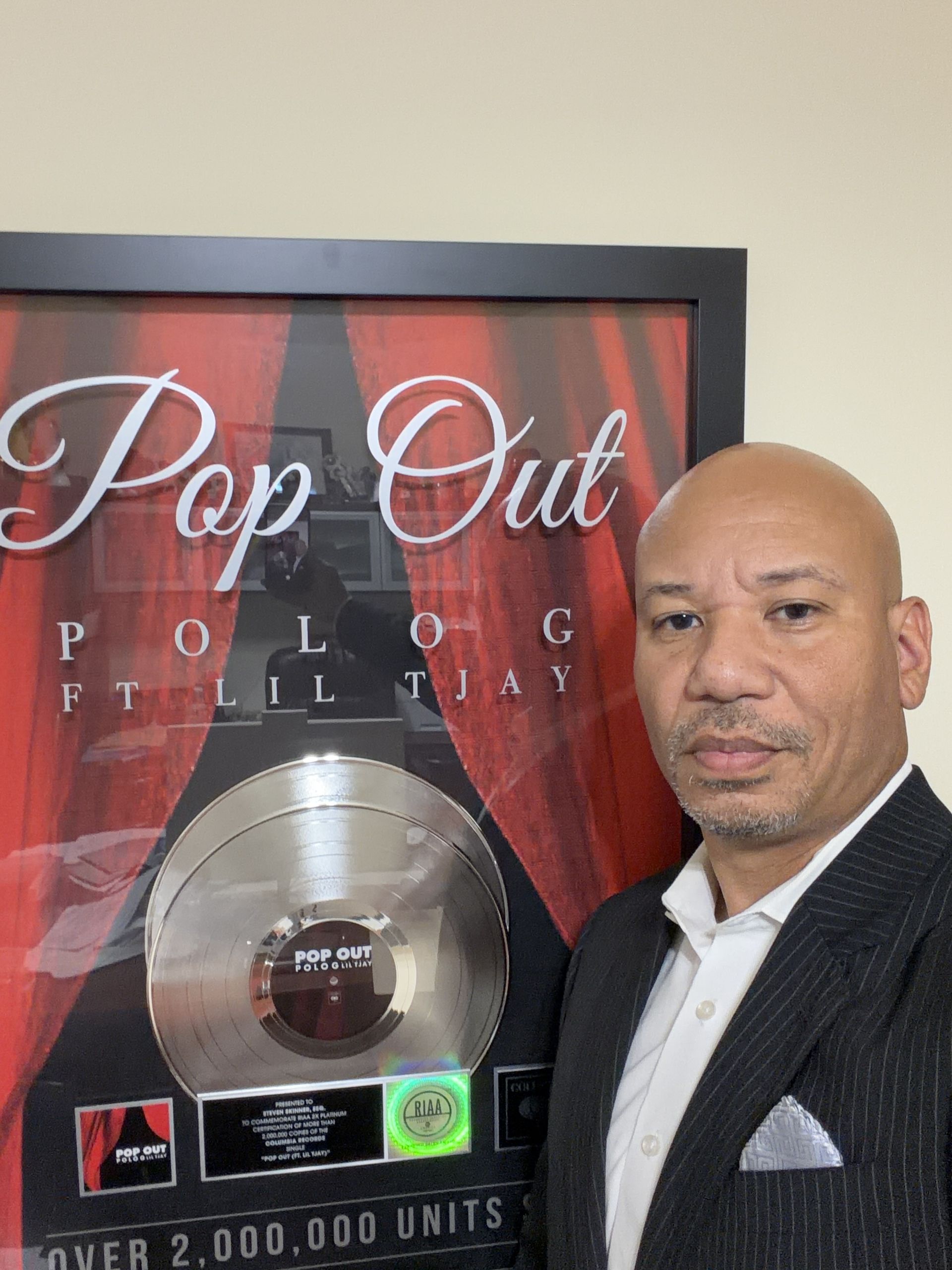 Man standing beside a framed “Pop Out” music award plaque with red and black background