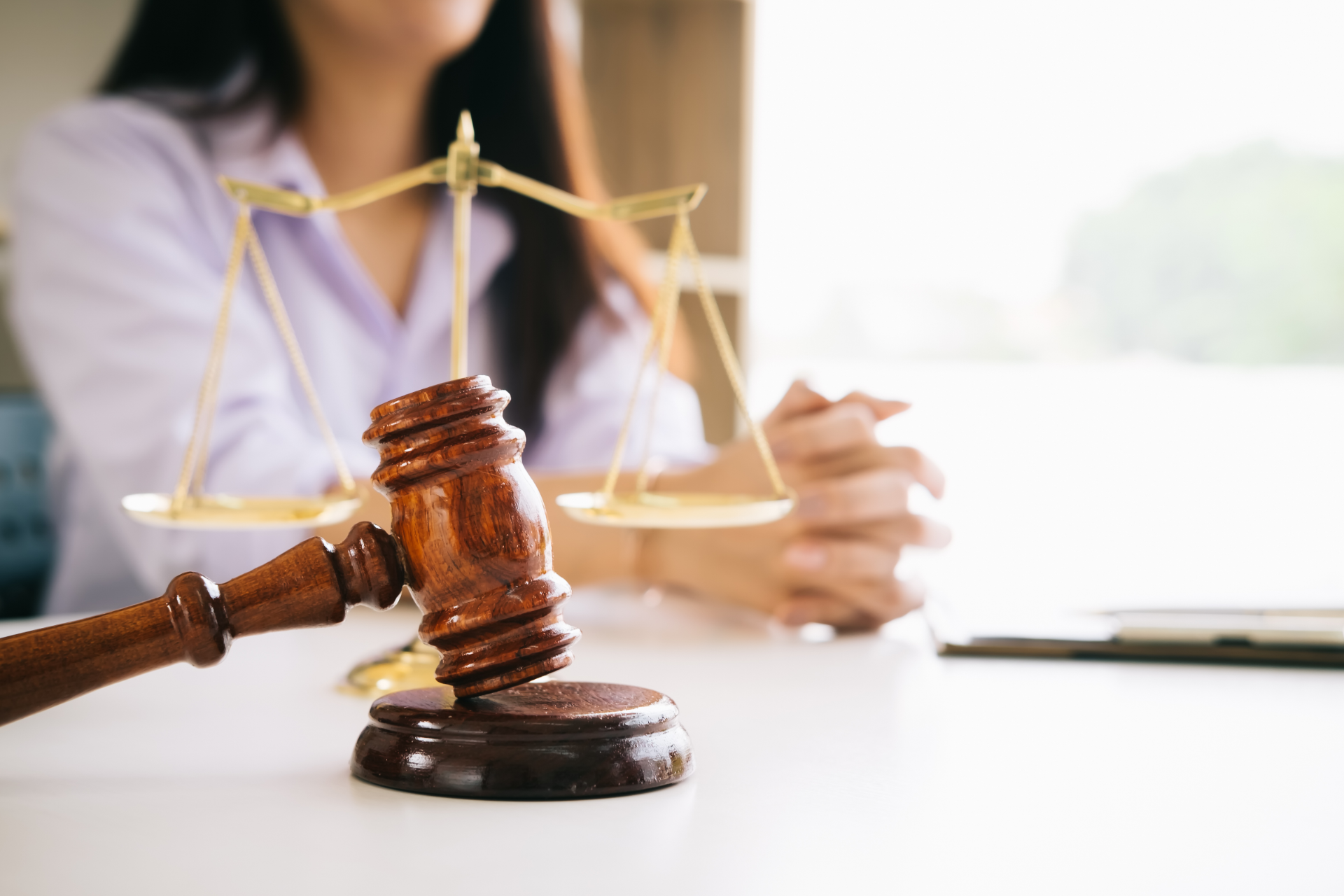 Justice gavel and scales on a desk with a blurred legal professional in the background