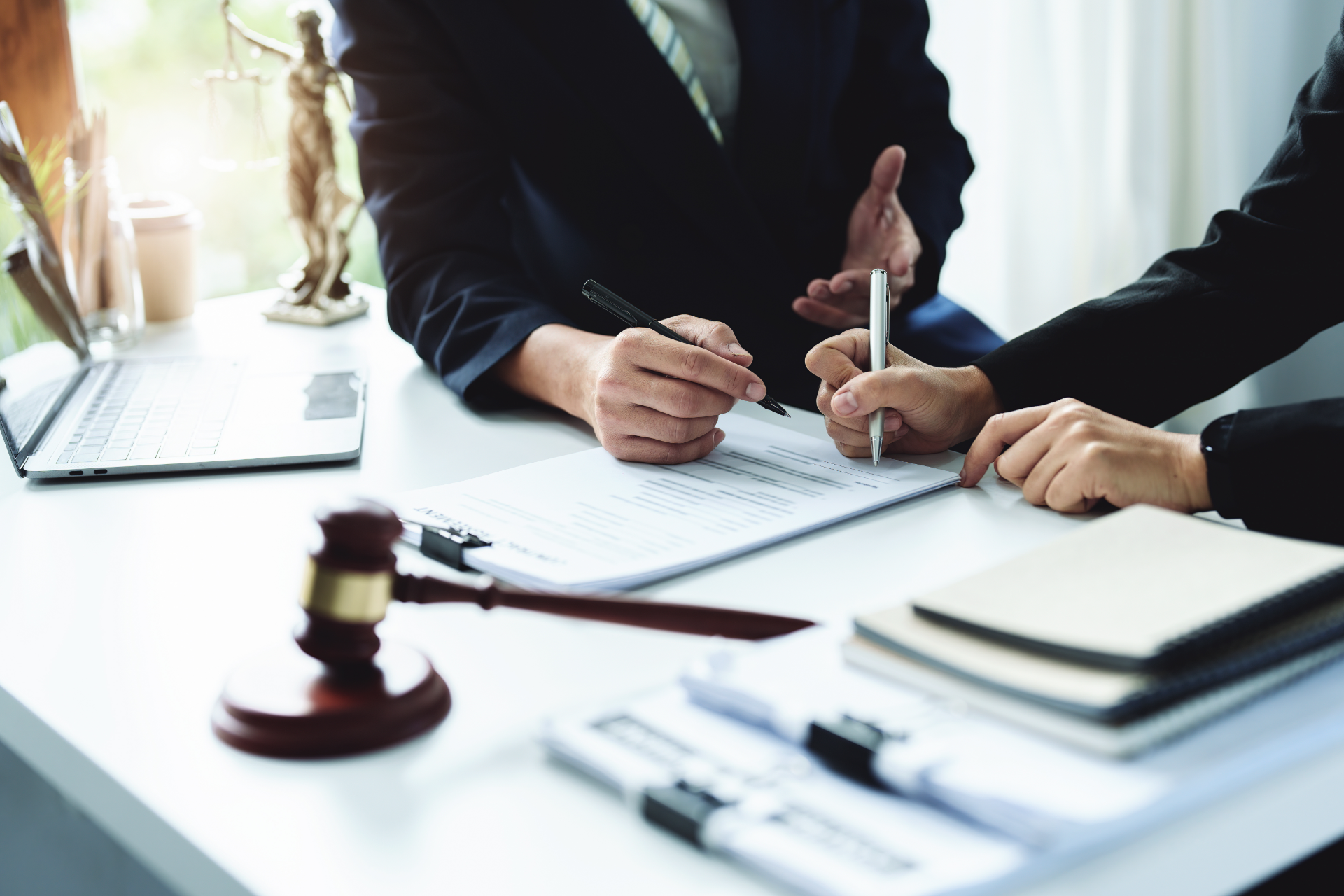 Lawyers signing documents at a desk with a gavel and laptop nearby