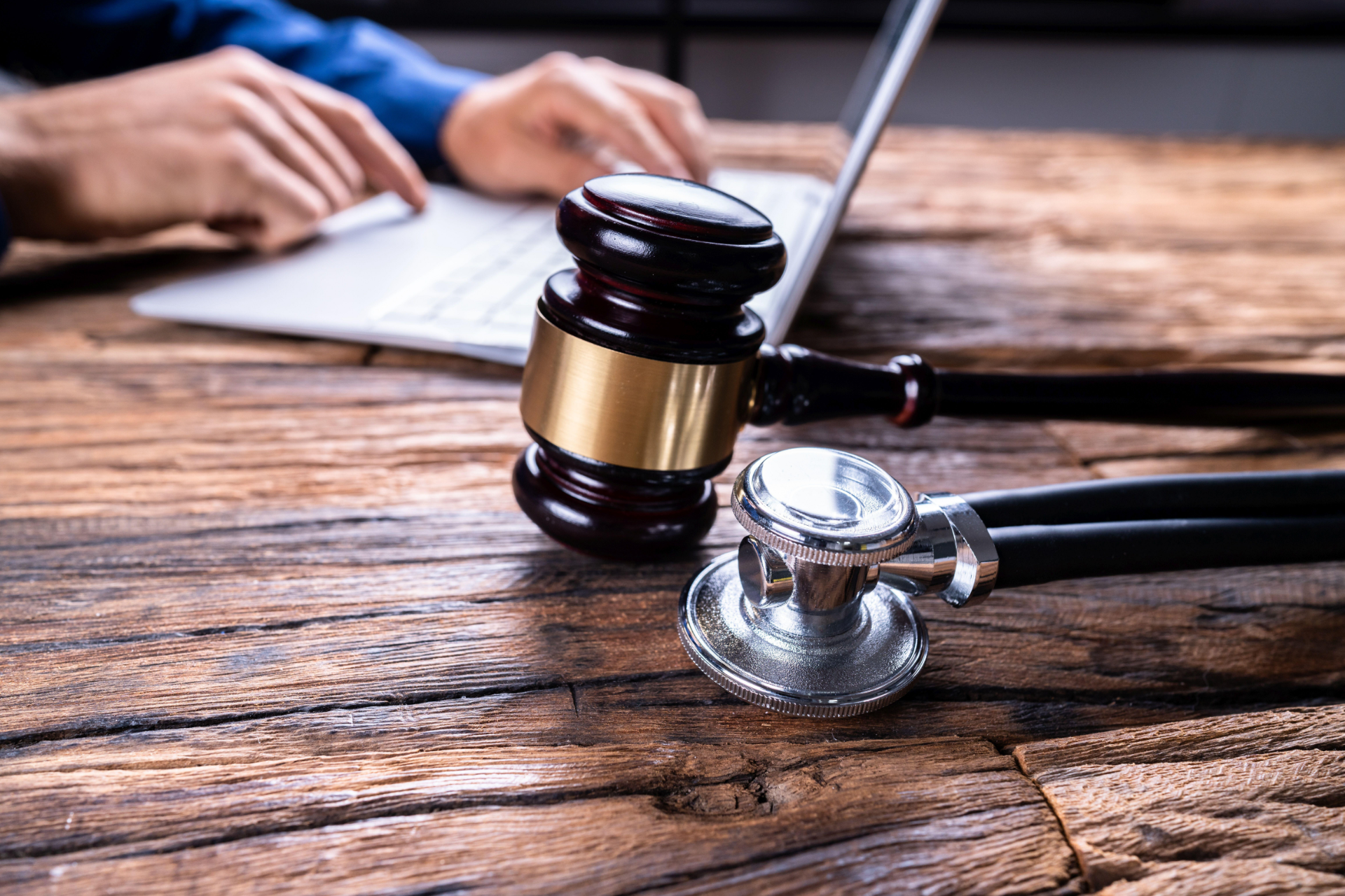 Lawyer’s desk with gavel, stethoscope, and hands typing on a laptop