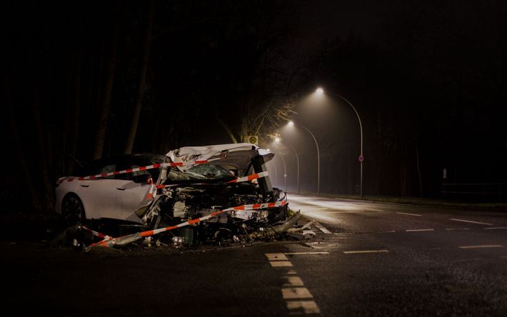 Severe car crash on a wet road at night, with a white vehicle mangled under streetlights