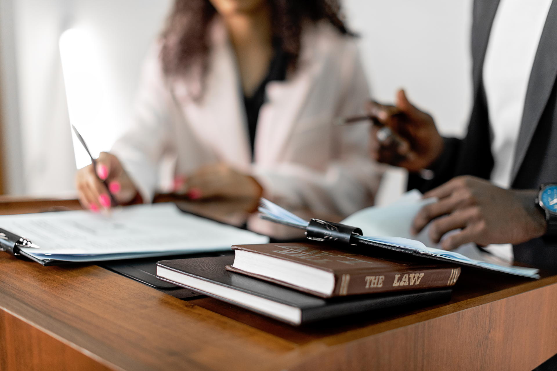 Two people in business attire review documents at a desk with notebooks and a pen