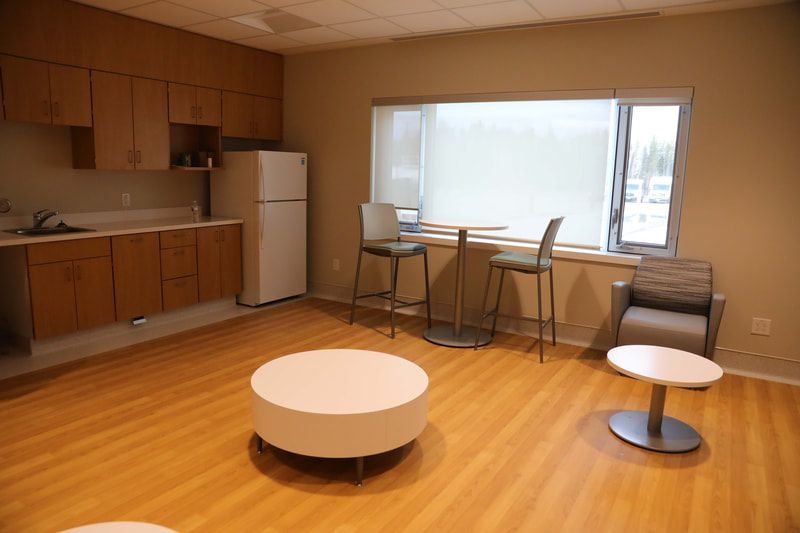 A living room with wooden floors , tables , chairs and a refrigerator.