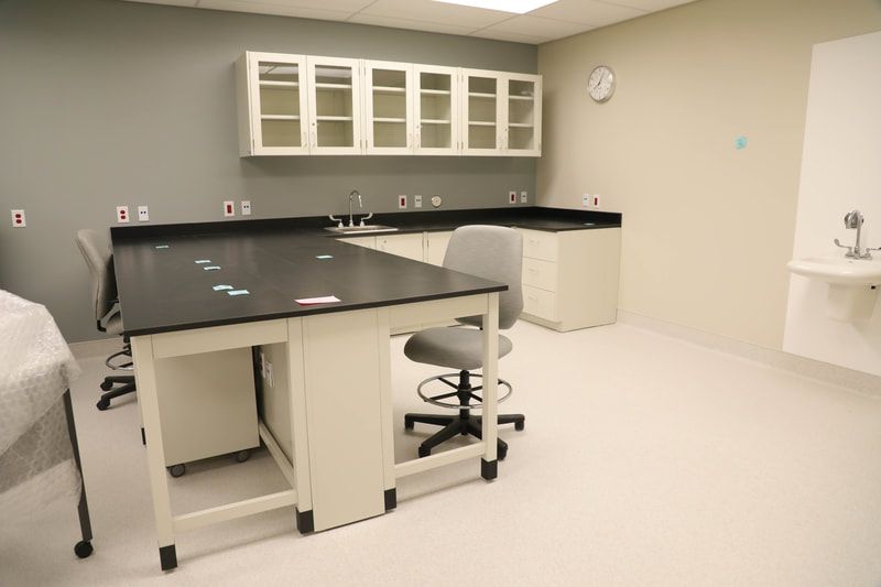 A laboratory with a table , chairs , cabinets and a sink.