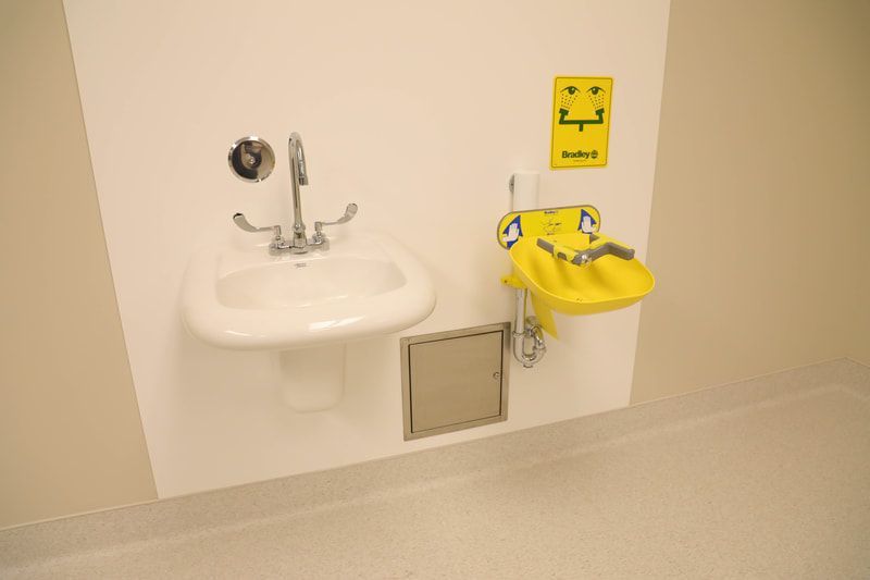 A bathroom with a sink and a yellow eye wash sink.