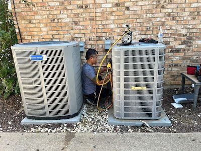 A man is working on two air conditioners in front of a brick building.