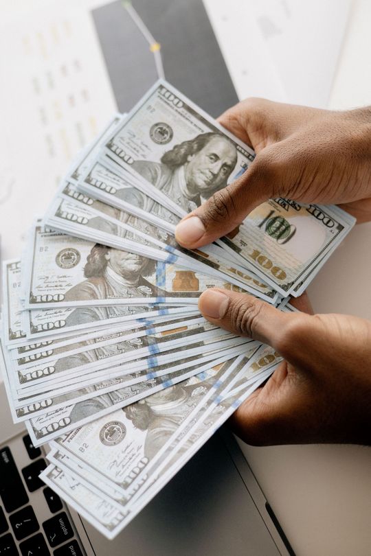 Hands fanning out multiple U.S. $100 bills over a laptop keyboard