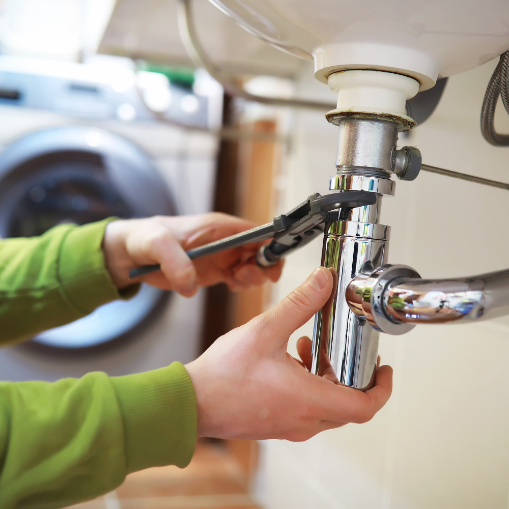 Person using a wrench to tighten a chrome pipe under a bathroom sink.