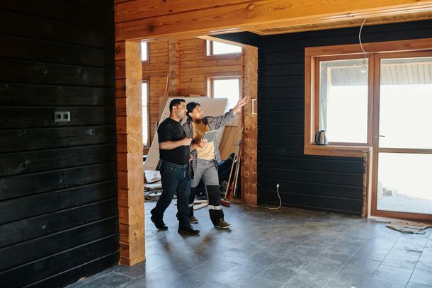 Two people inside a building, one pointing at window; interior with exposed wooden beams, dark walls.