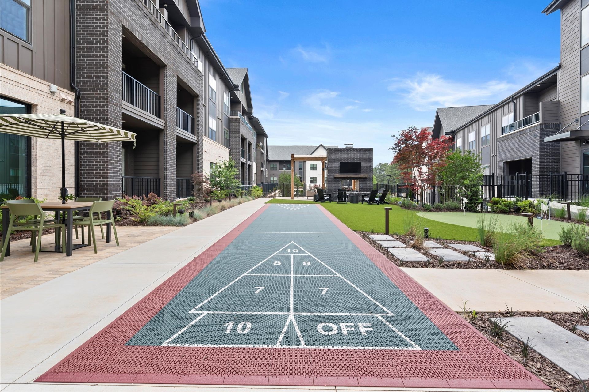 Shuffleboard court in outdoor courtyard, between apartment buildings, blue sky.