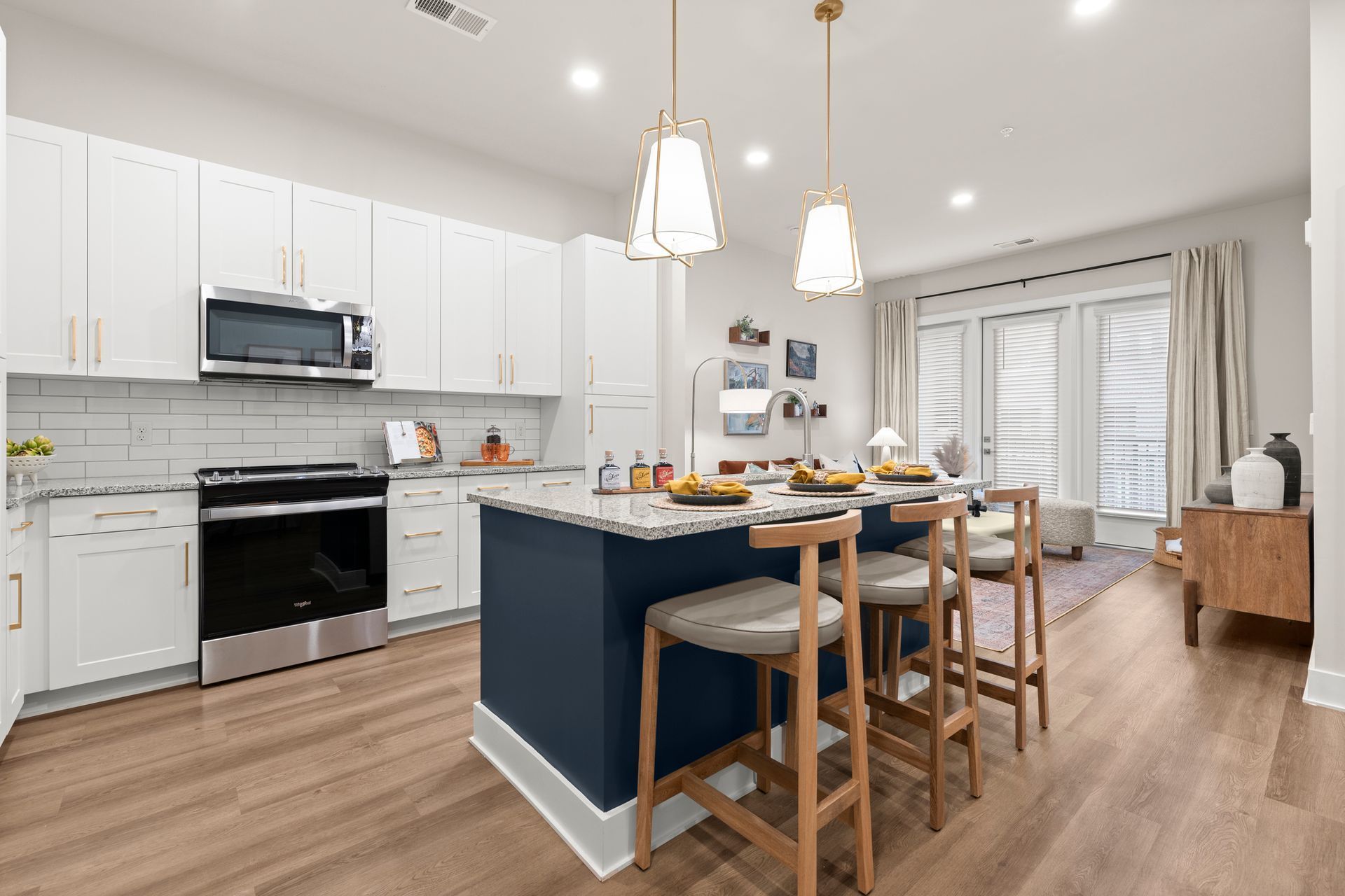 Modern kitchen with white cabinets, blue island, granite countertops, and wood floors.