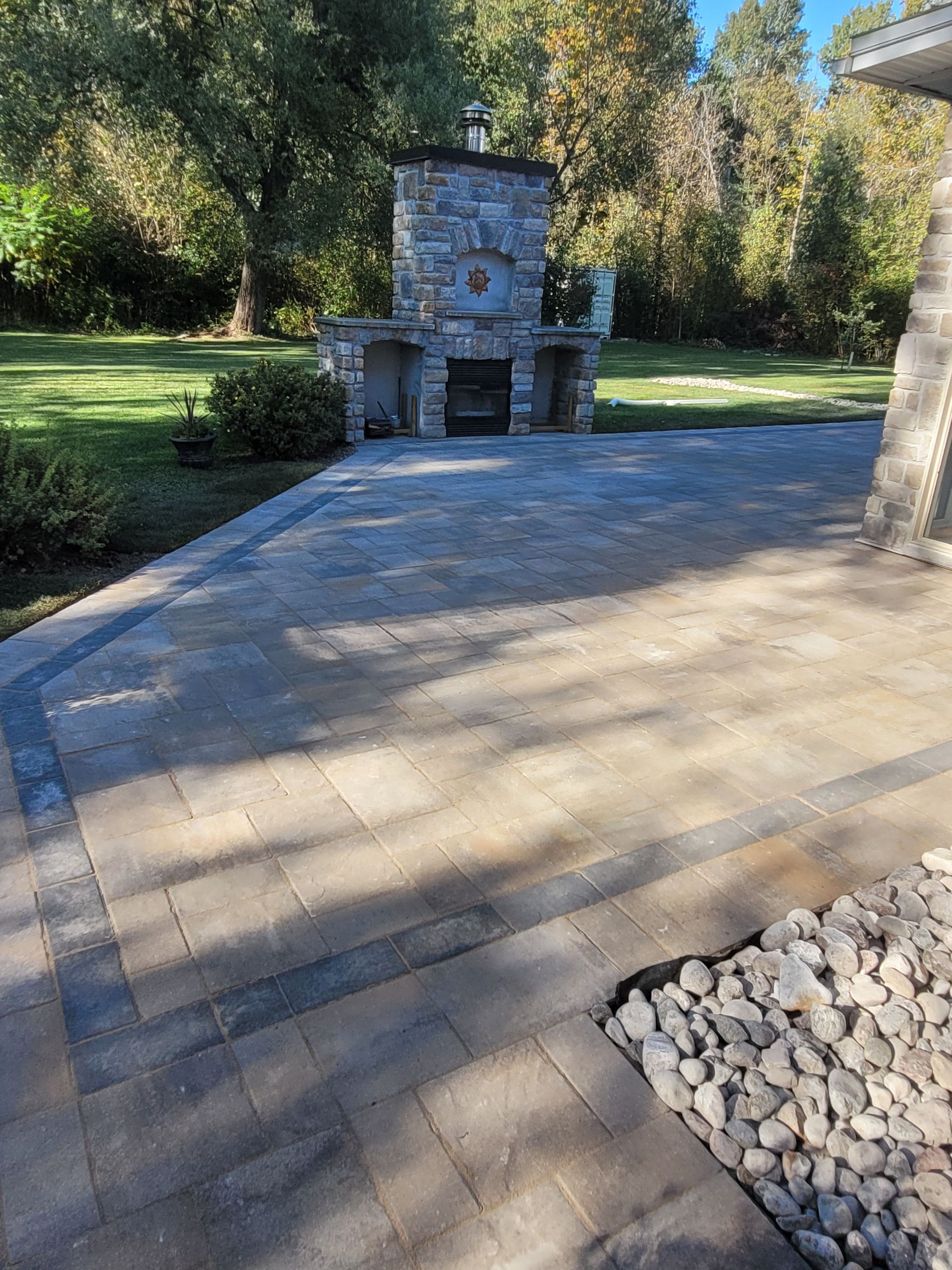 Stone patio with outdoor fireplace; rocks and grass in background.