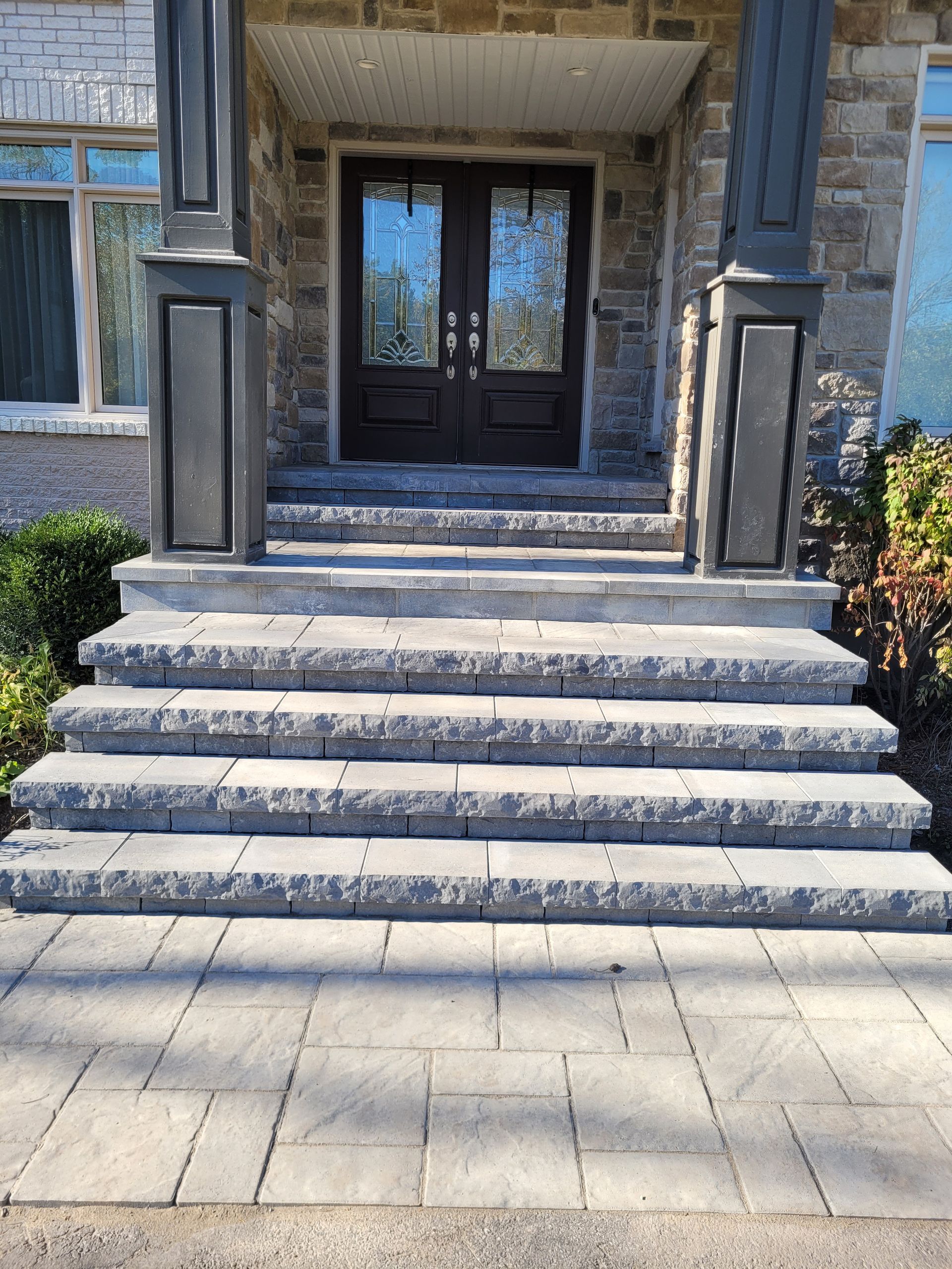 Stone steps lead to a dark double door entrance, flanked by pillars and a paved walkway.
