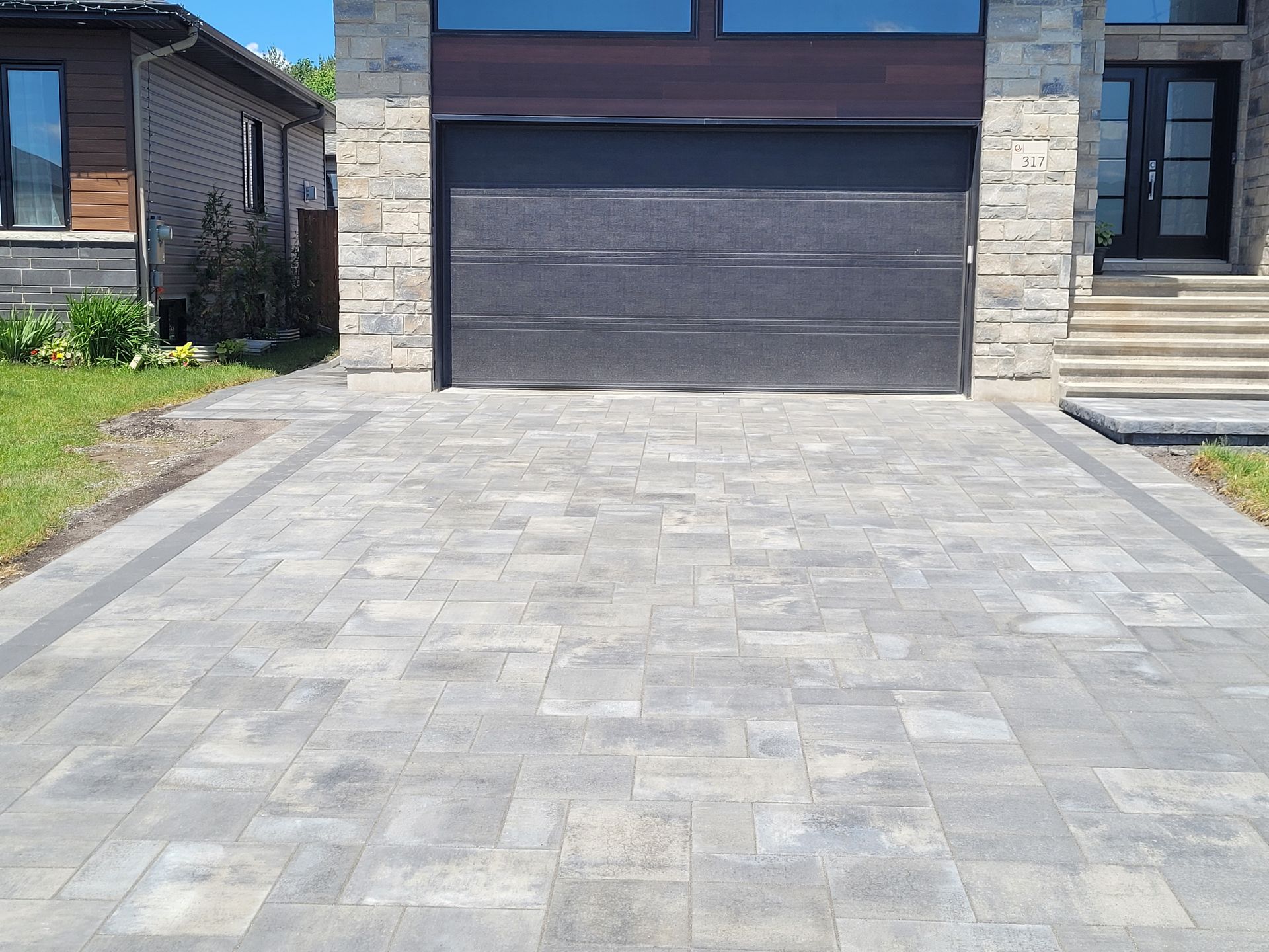 Gray paver driveway leading to a garage with a dark gray door and stone facade.