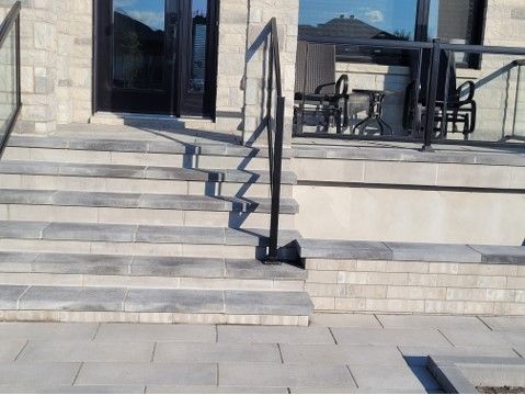 Stone steps leading up to a house entrance with a black metal handrail and glass panels.