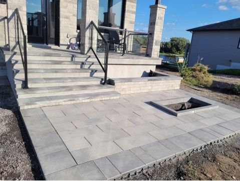 Grey paver patio with stairs and a built-in fire pit; view of a house in the background.