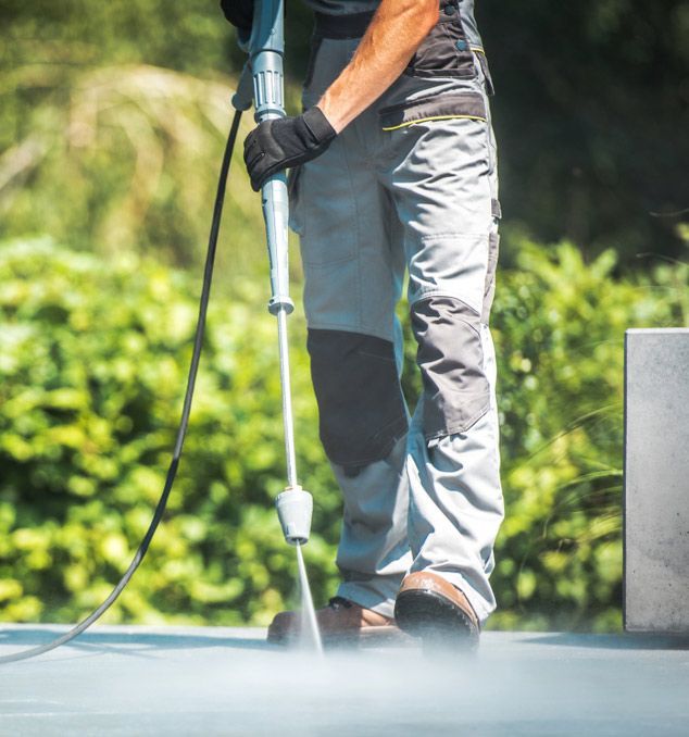 A Man Is Using A High Pressure Washer To Clean A Concrete Surface — Porta-Vac in Cannonvale, QLD