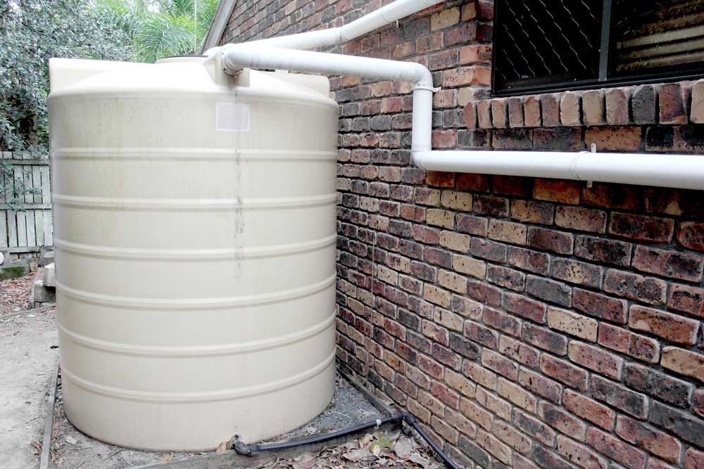 A Large White Water Tank Is Sitting Next To A Brick Wall — Porta-Vac in Airlie Beach, QLD