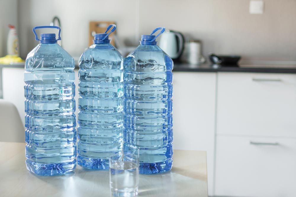 Three Bottles Of Water And A Glass Of Water On A Table In A Kitchen — Porta-Vac in Moranbah, QLD