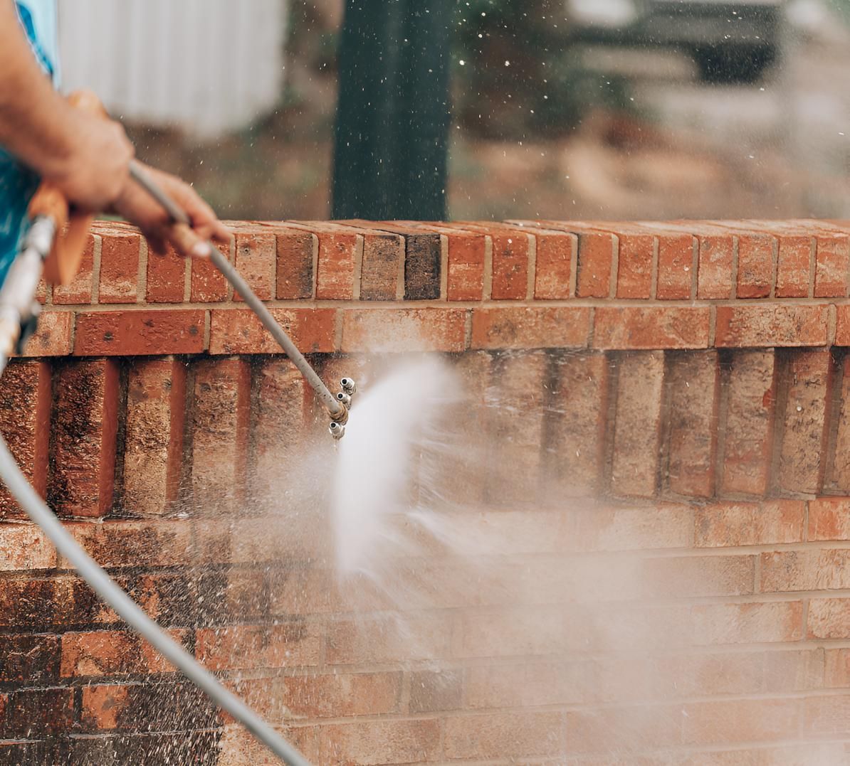 A Person is Using a High Pressure Washer to Clean a Brick Wall — Porta-Vac in Cannonvale, QLD