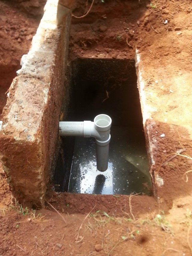 A rectangular hole in the ground lined with concrete, containing water and a vertical PVC pipe.