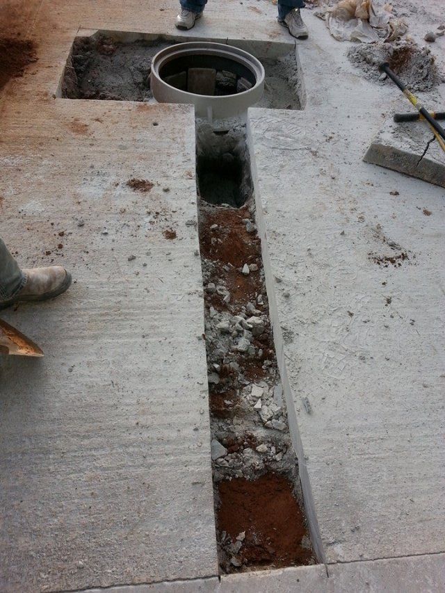 Workers excavating concrete around a manhole, creating a trench.