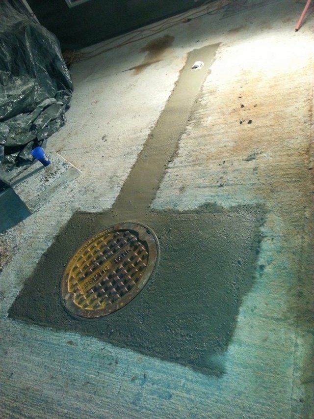 Manhole cover surrounded by fresh concrete on a sidewalk. Yellow cover, gray concrete, and weathered sidewalk.