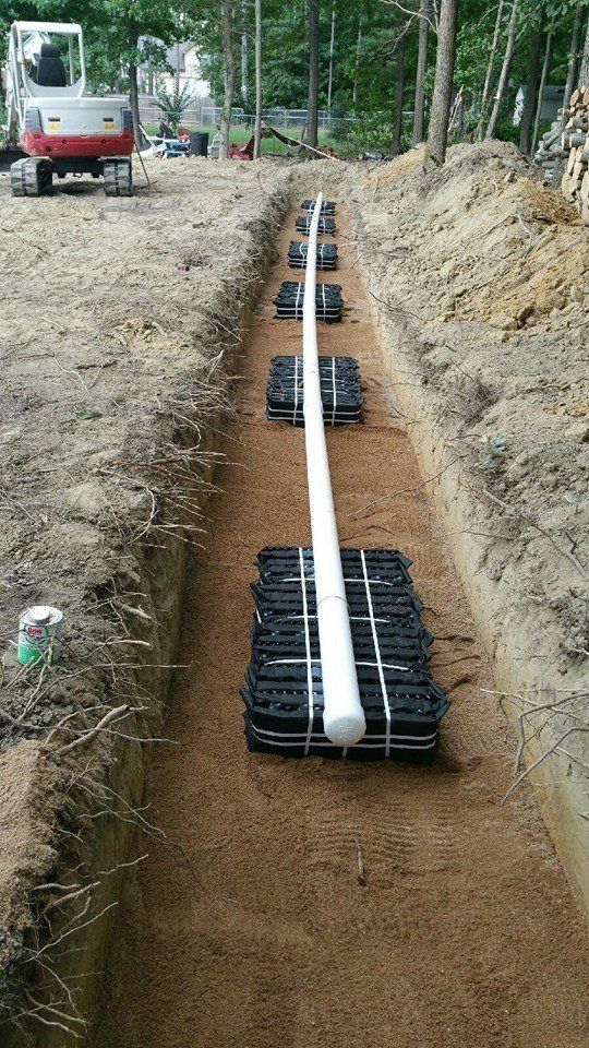 Trench with a white pipe and black plastic structures laid in a bed of tan gravel; construction site.