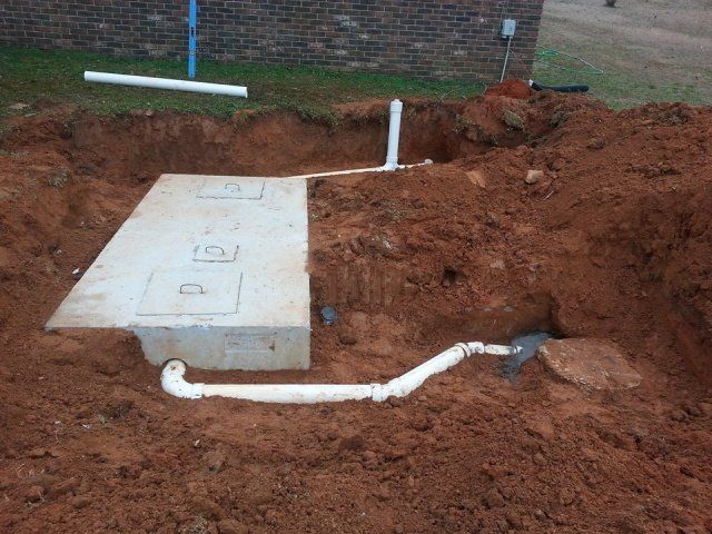 A concrete septic tank partially buried in dirt, with connecting pipes.