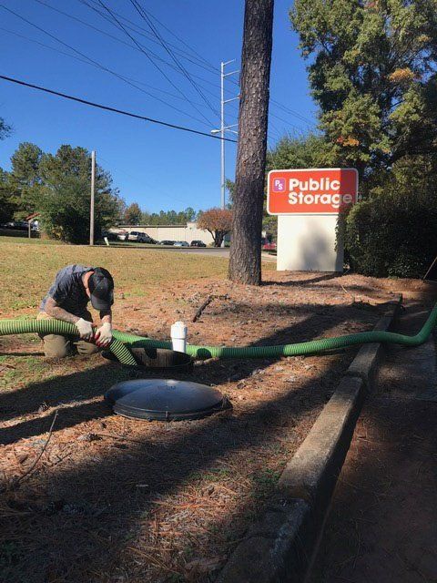 Man connecting a hose to a septic tank near a Public Storage sign on a sunny day.