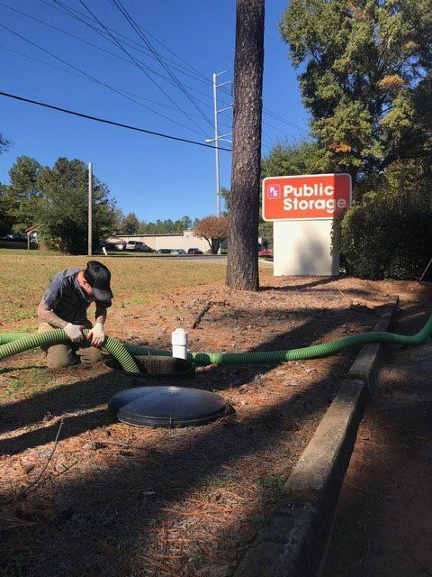 Man connecting green hoses to a storage tank outside a Public Storage facility on a sunny day.