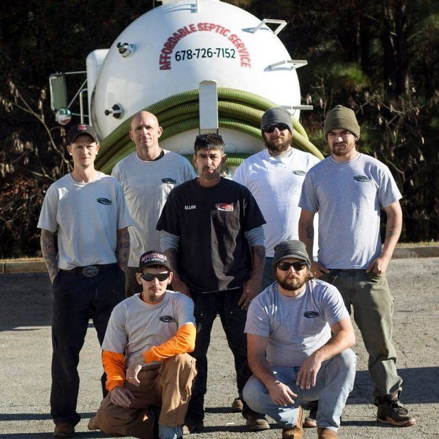 Septic service crew posing in front of their truck. Crew members wear work clothes.