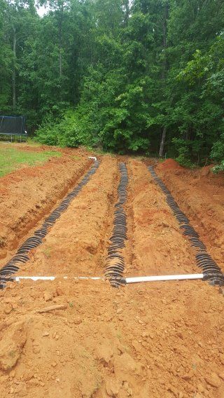 Trenches dug in soil with black plastic septic system components, outdoors.