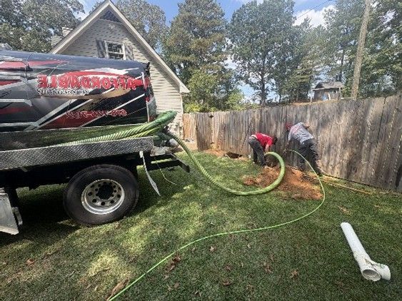 Two workers pumping septic tank with truck in residential yard.