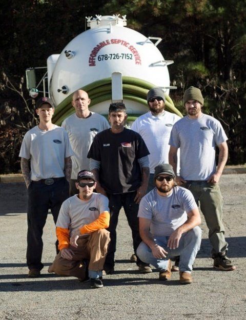 Septic service crew posing in front of their truck. Men in uniform with the company logo.
