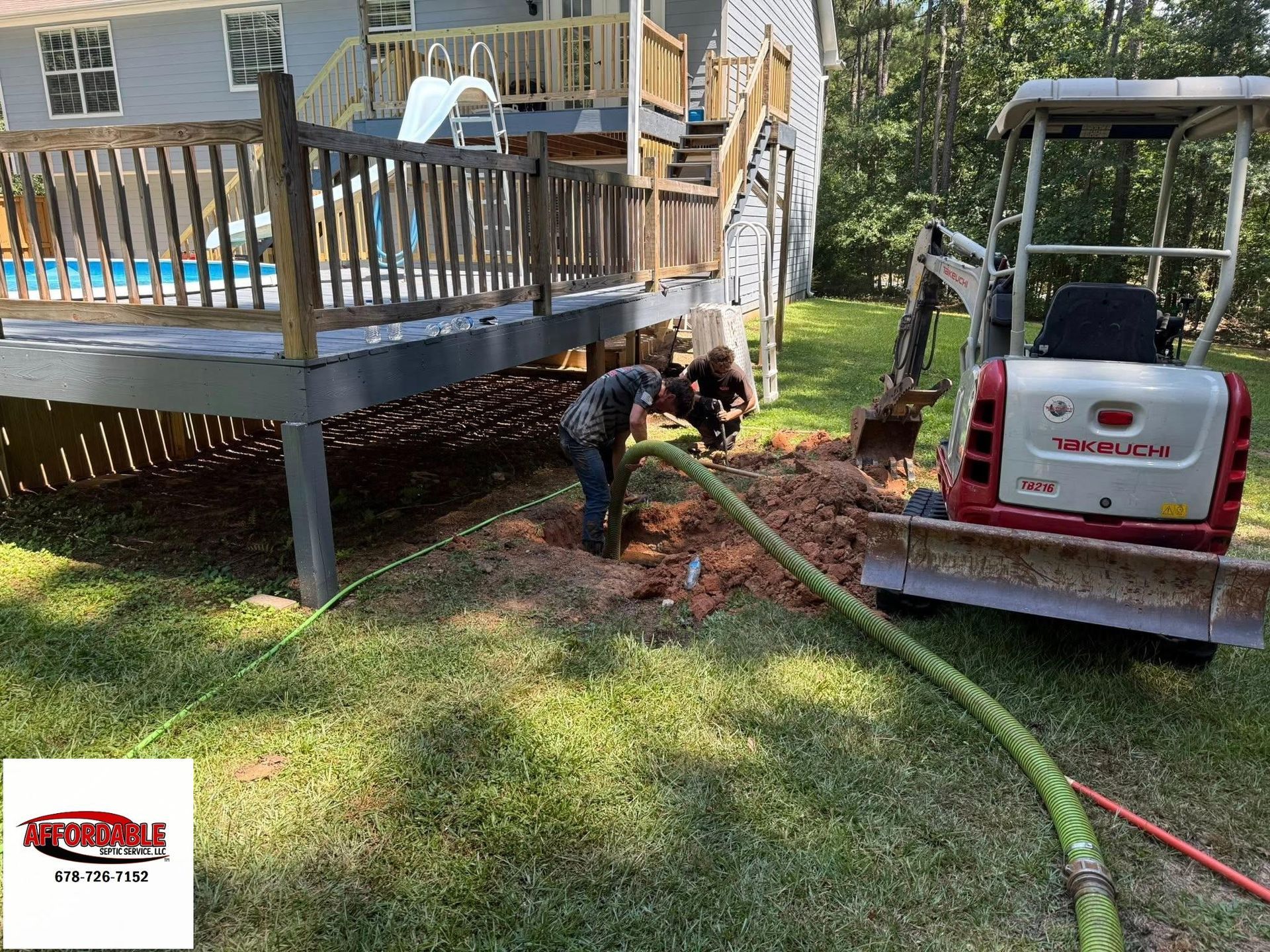 Technicians repair septic system using hose and mini excavator beside a raised backyard deck.