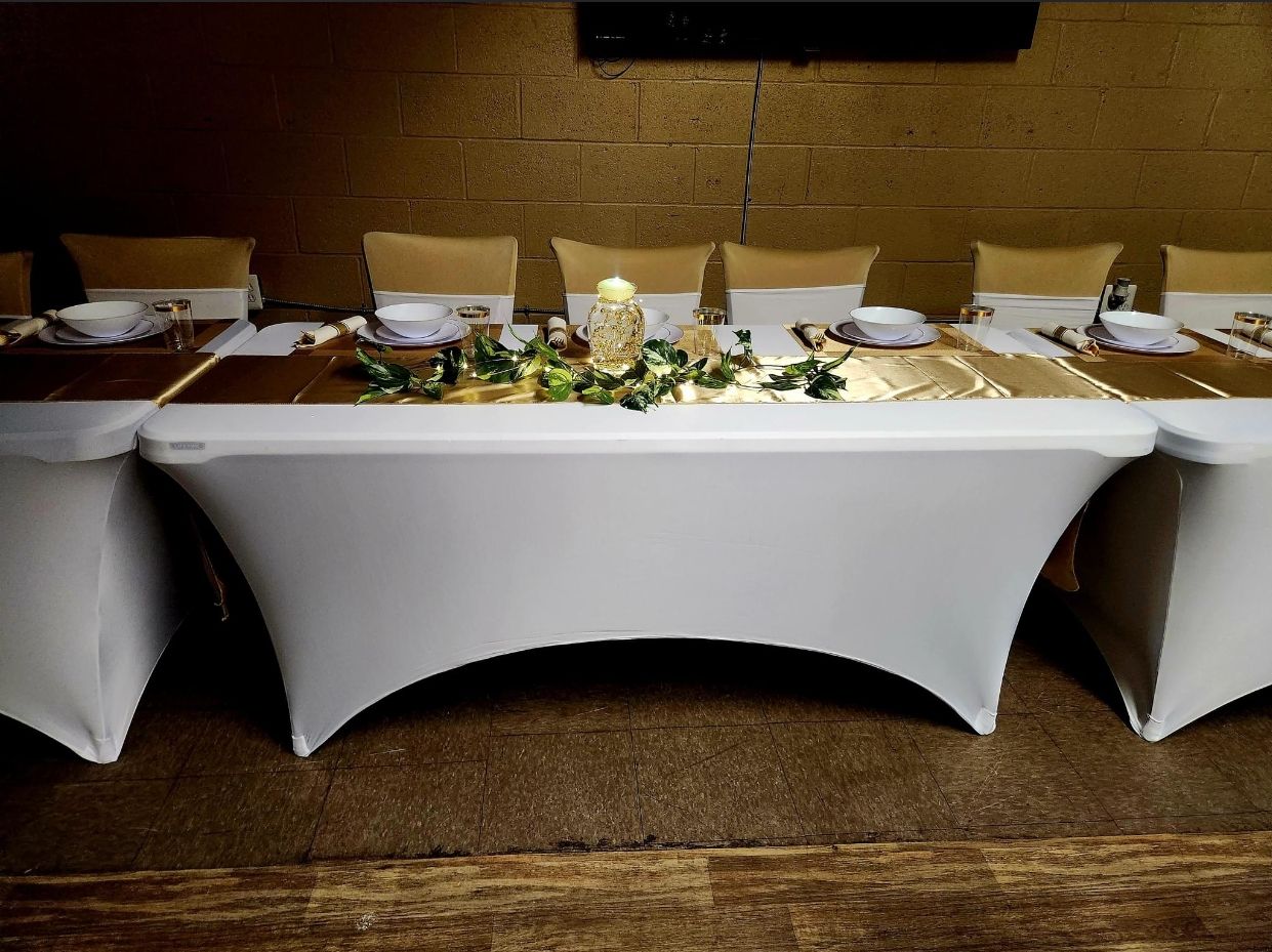 White-covered tables with gold table runners and decorations, set for a formal event, with gold-covered chairs.