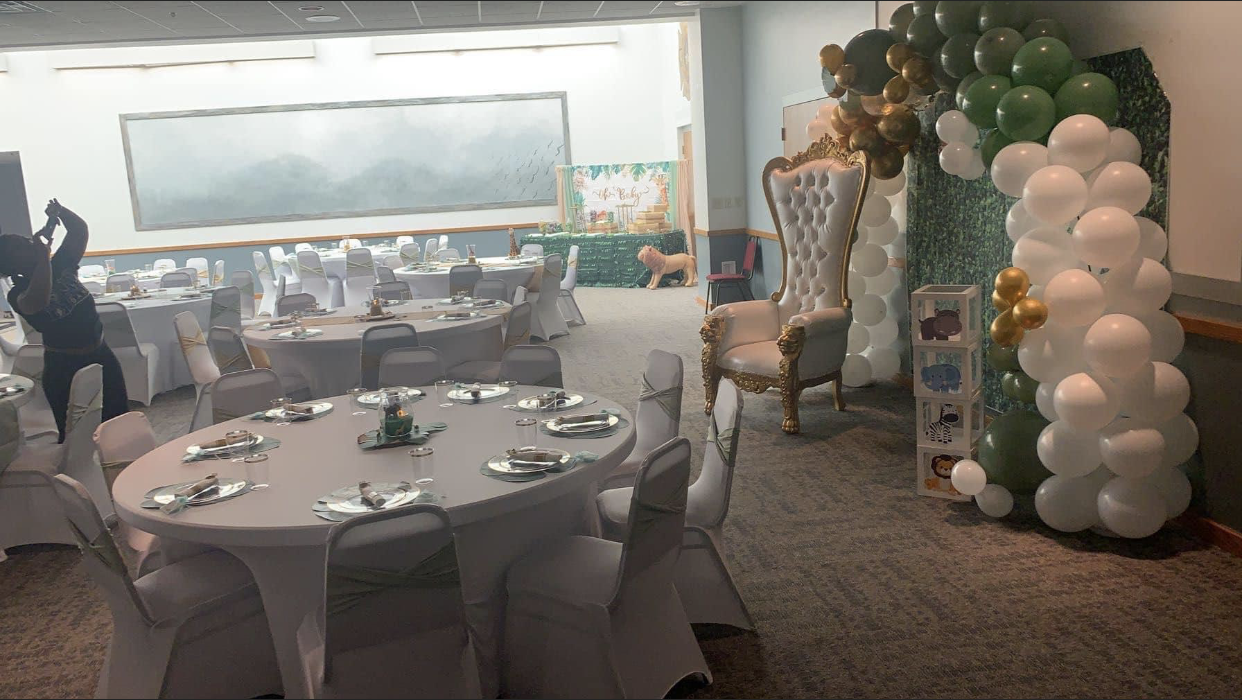 A banquet hall set for an event; round tables with white linens, chairs, and balloon decorations.