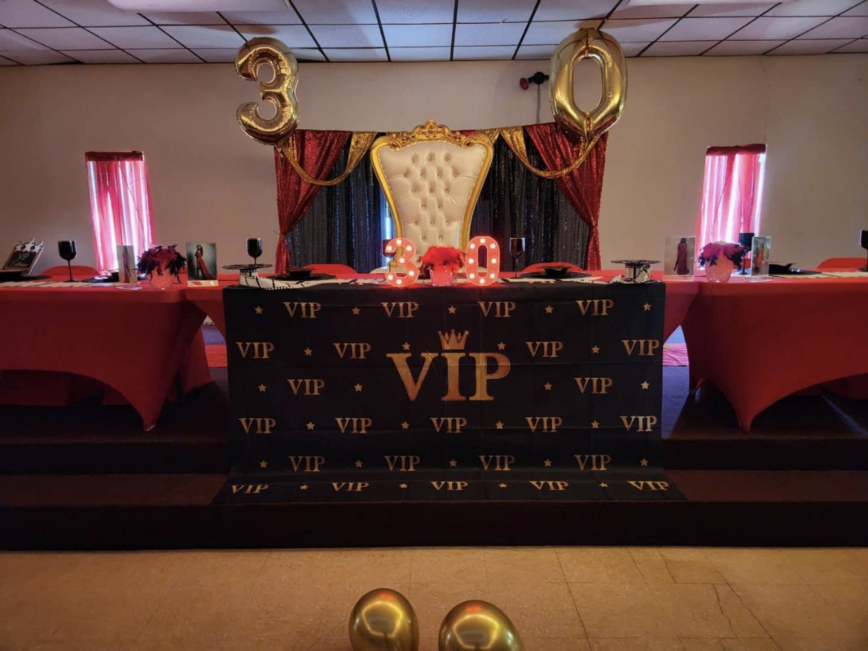 A VIP party setup for a 30th birthday, featuring a throne, red and gold decor.