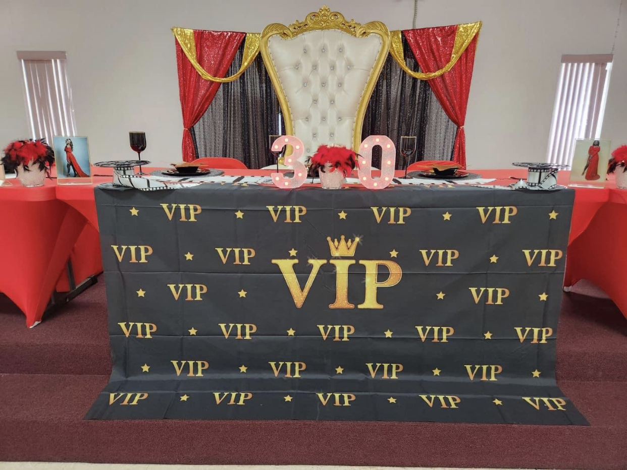 A VIP-themed 30th birthday party setup with a throne, black and gold decor, and red accents.