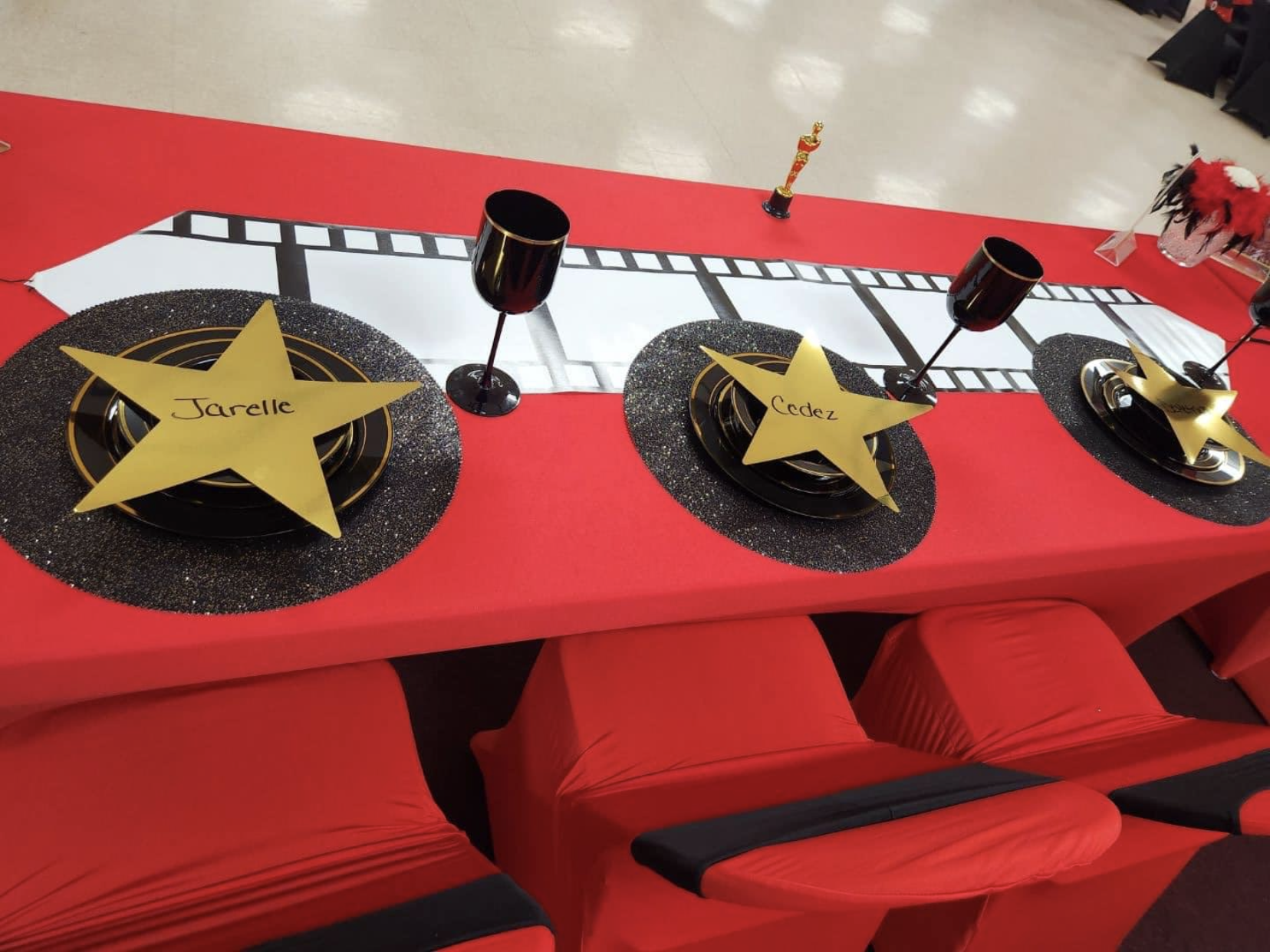 Red carpet-themed table setting with gold star place cards, film strip runner, black chairs.