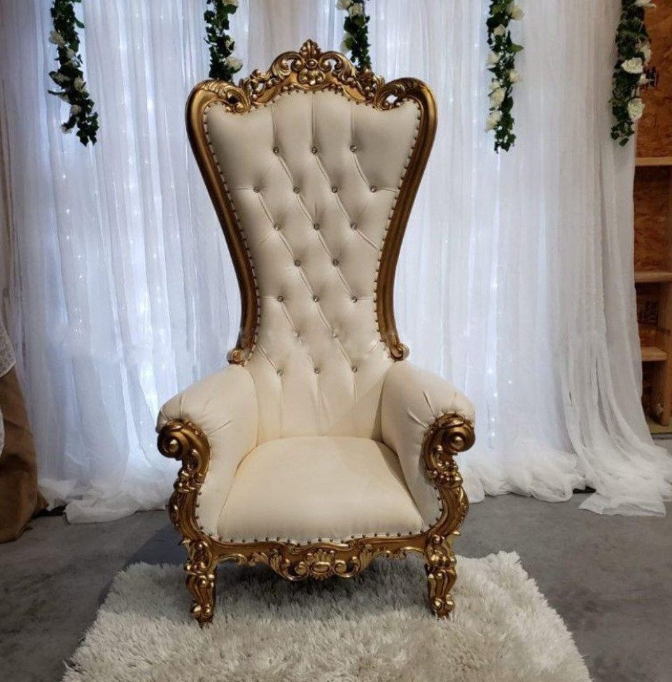 Ivory and gold throne chair on a white rug, set against a white curtain backdrop with floral accents.