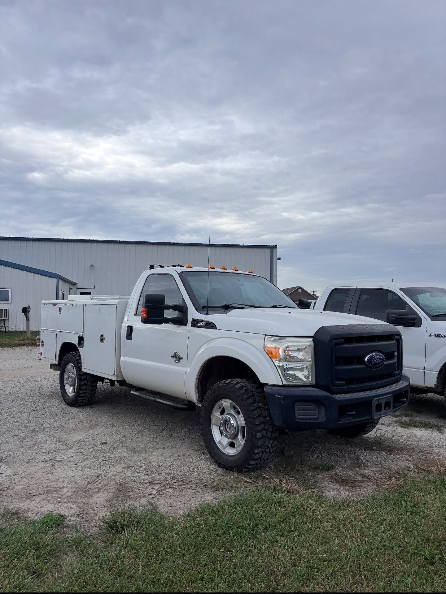 White utility truck parked on gravel beside a warehouse under a cloudy sky