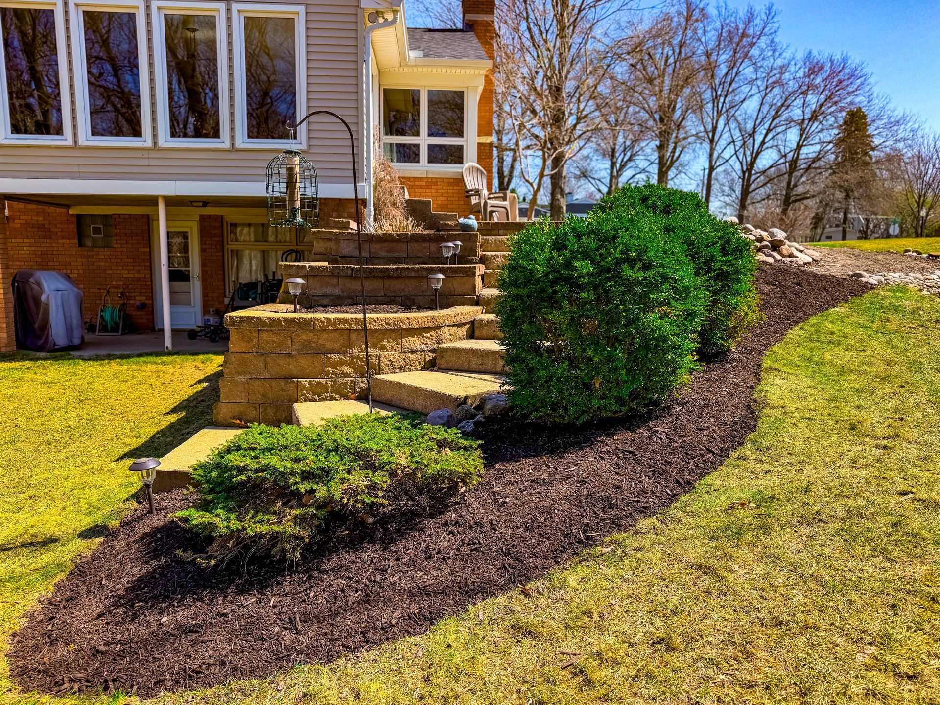 Backyard stone steps beside a house with a trimmed shrub and fresh mulch bed